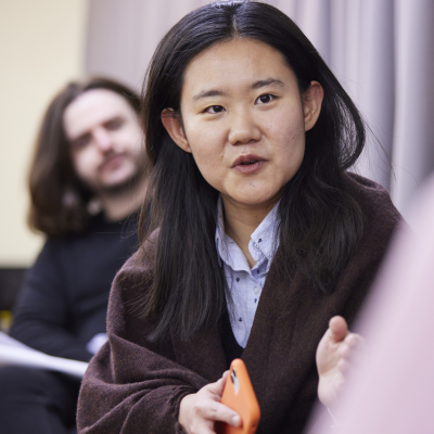 An Asian woman wearing a blue shirt speaks about her research